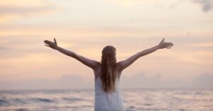 A woman with her arms stretched out wide looking out towards the ocean.